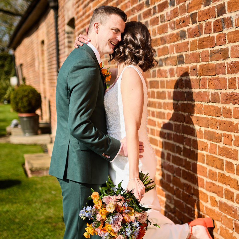 Bride and groom embracing against a red-brick wall at Hatfield Place, Essex