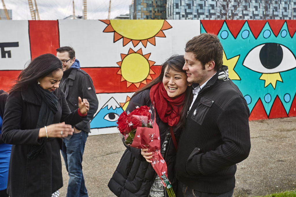 Newly engaged couple laughing with friends in front of a colourful mural
