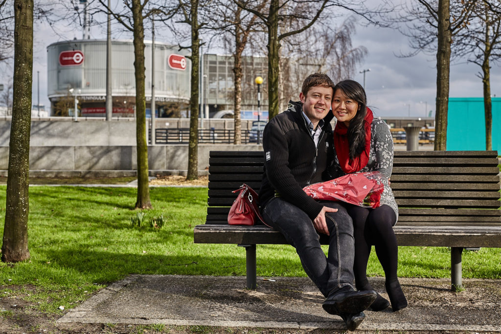 Newly engaged couple sitting on a park bench with red roses