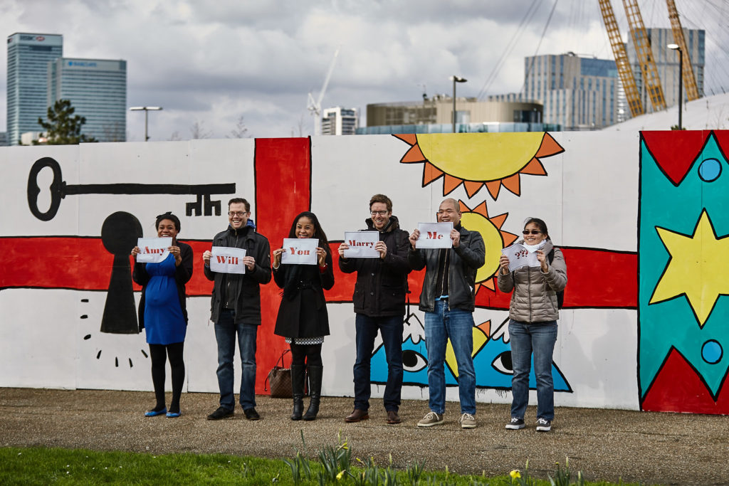 Friends lined up with proposal signs in front of a colourful mural