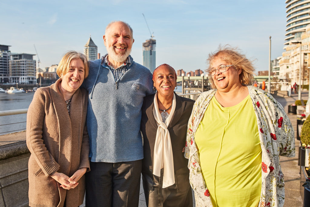 Four friends smiling arm in arm on the riverside terrace at Vauxhall