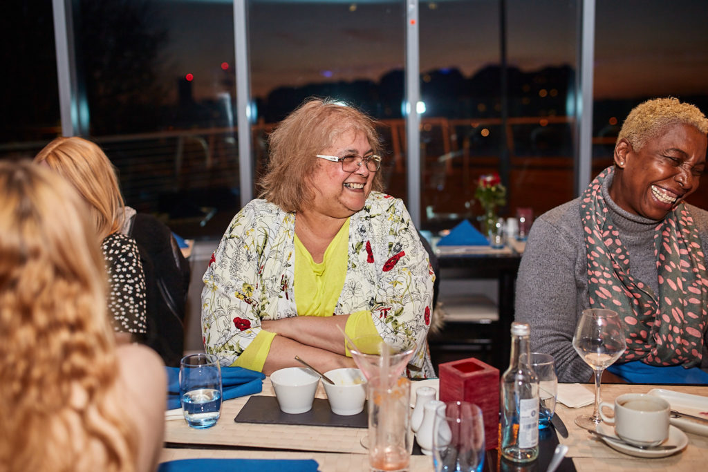 Two guests smiling at the table beside the window at dusk