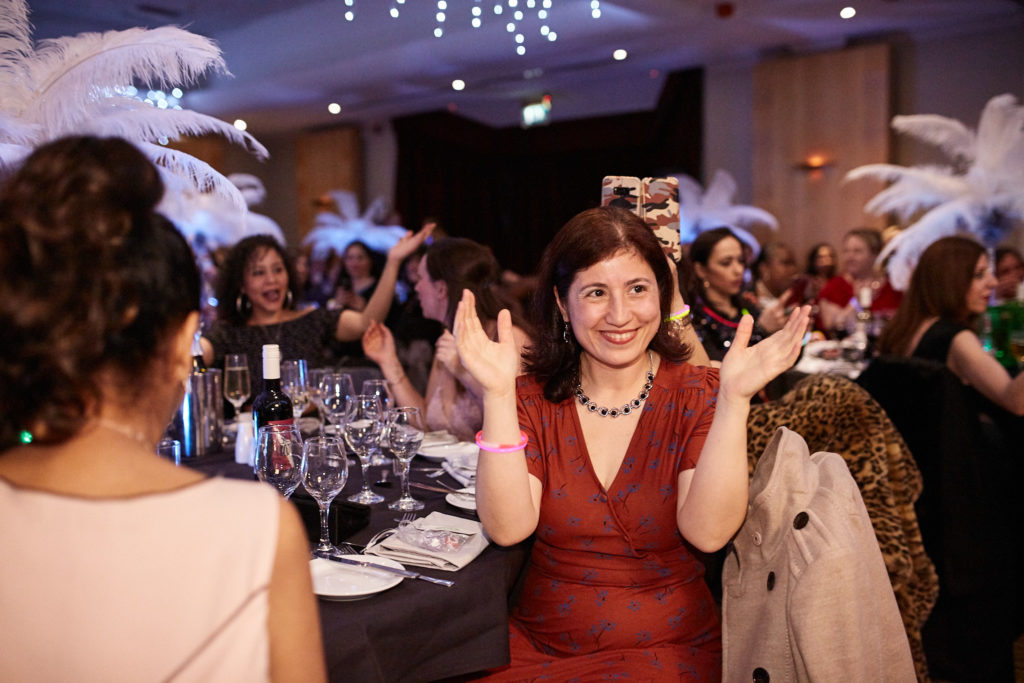 Guest in a red dress laughing with her arms out at the table