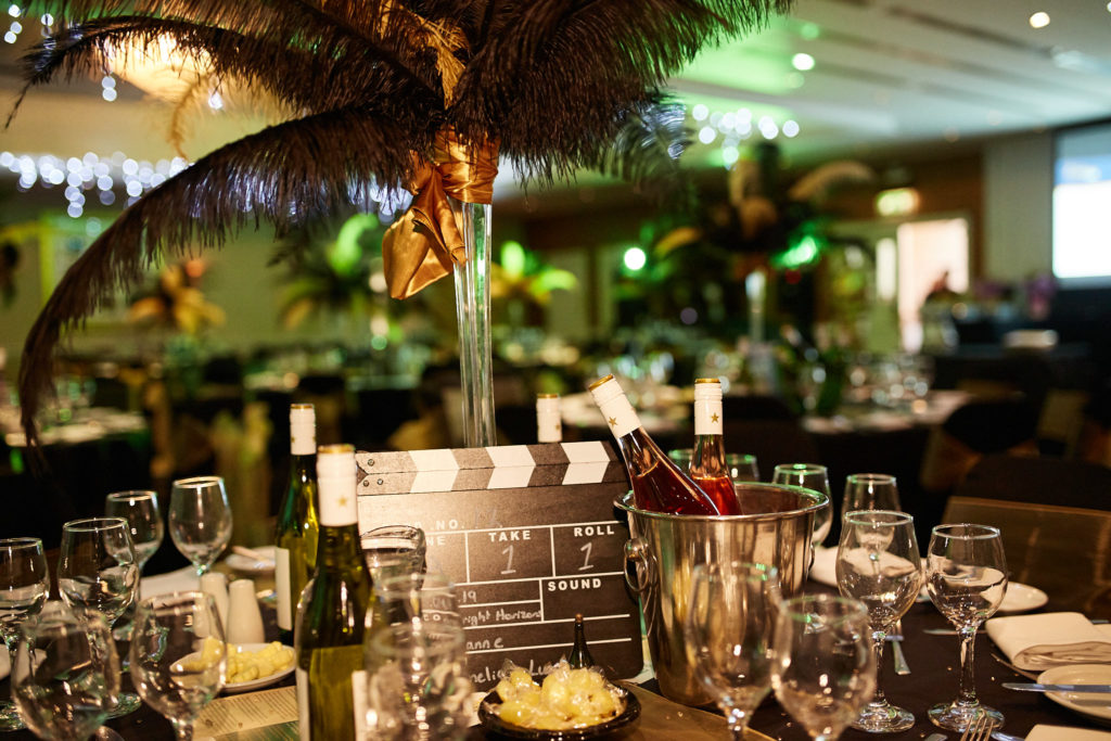 Awards dinner table set with a black feather centrepiece and a clapperboard