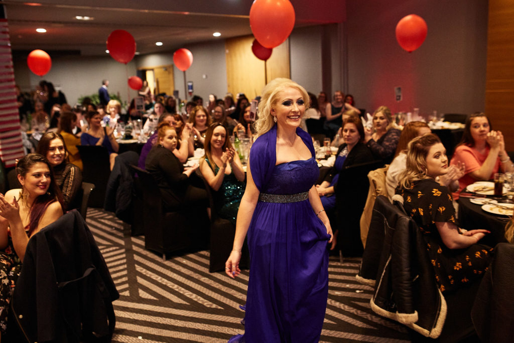 Award winner in a purple dress walking between the tables
