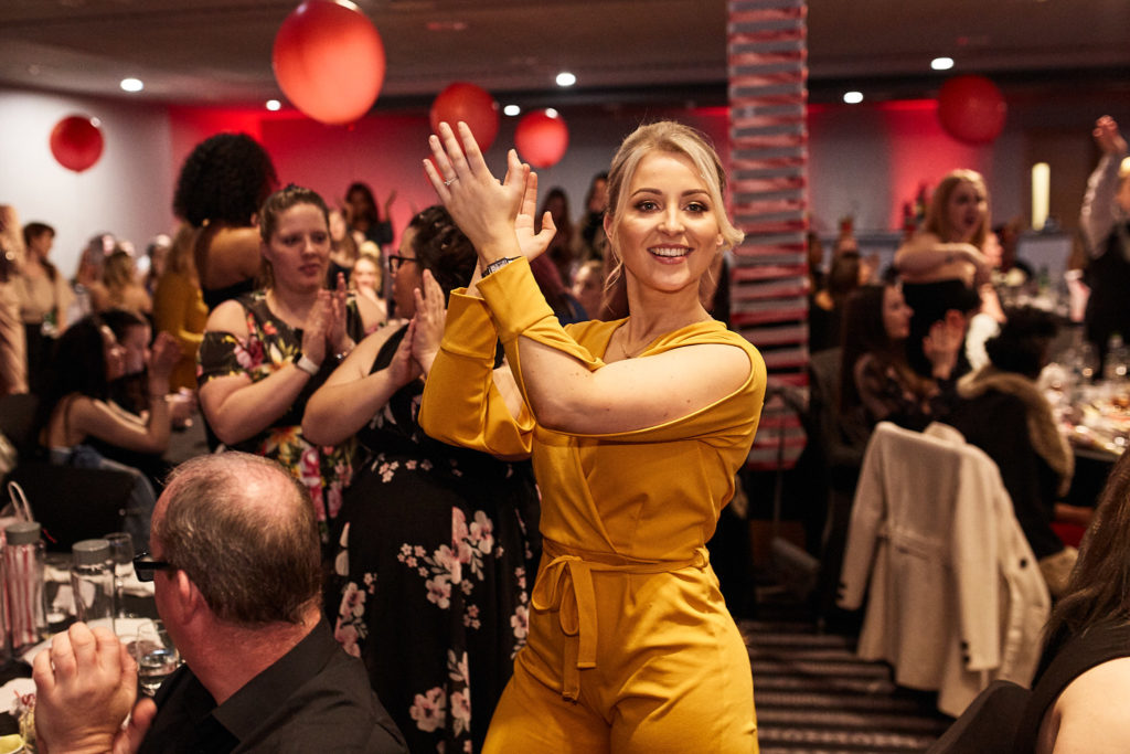 Guest in a yellow outfit waving as she walks through the room