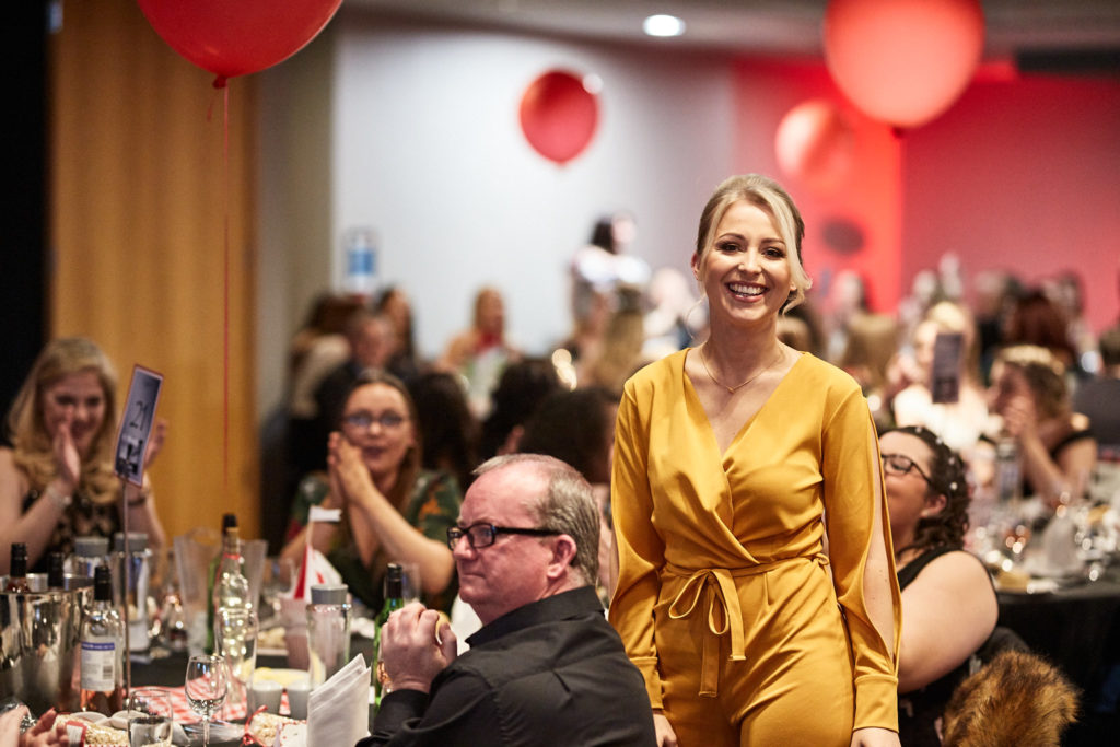Guest in a yellow dress smiling as she stands among the tables
