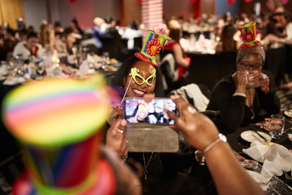 Guest in a novelty rainbow hat taking a photo at the table