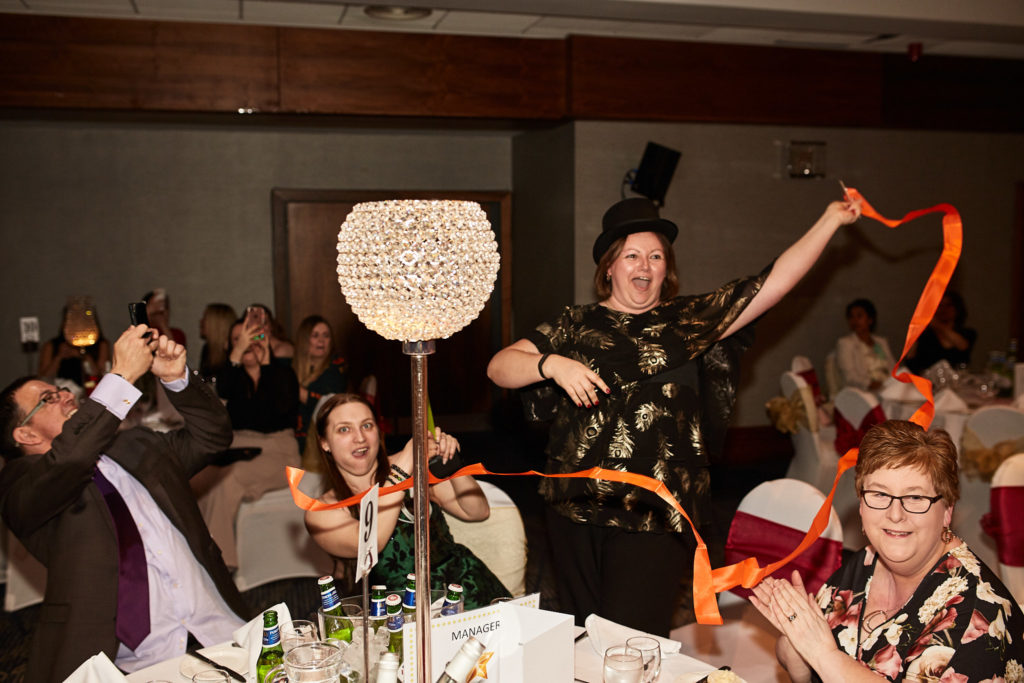 Guests in top hats waving ribbons at their table at an awards evening at the Wembley Holiday Inn