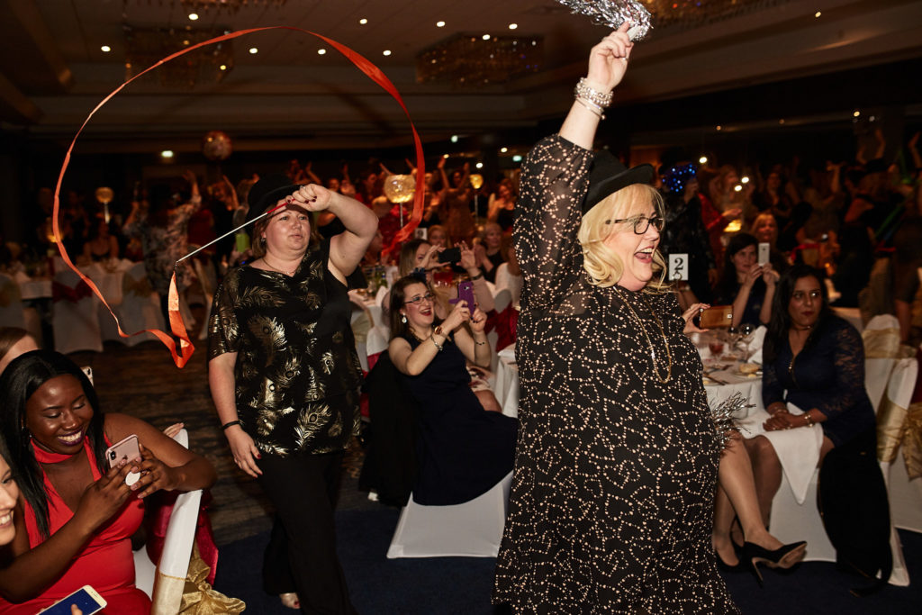 Guest in a top hat twirling a ribbon as her table cheers