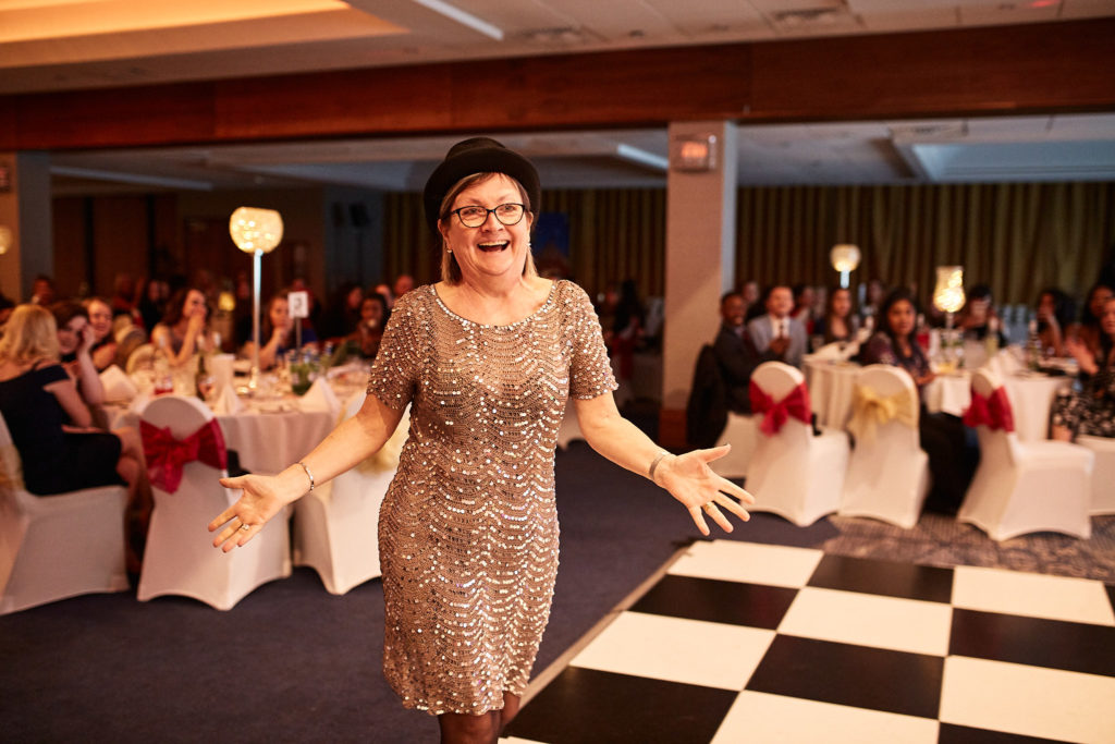 Award winner in a sequinned dress walking across the dance floor with her arms out