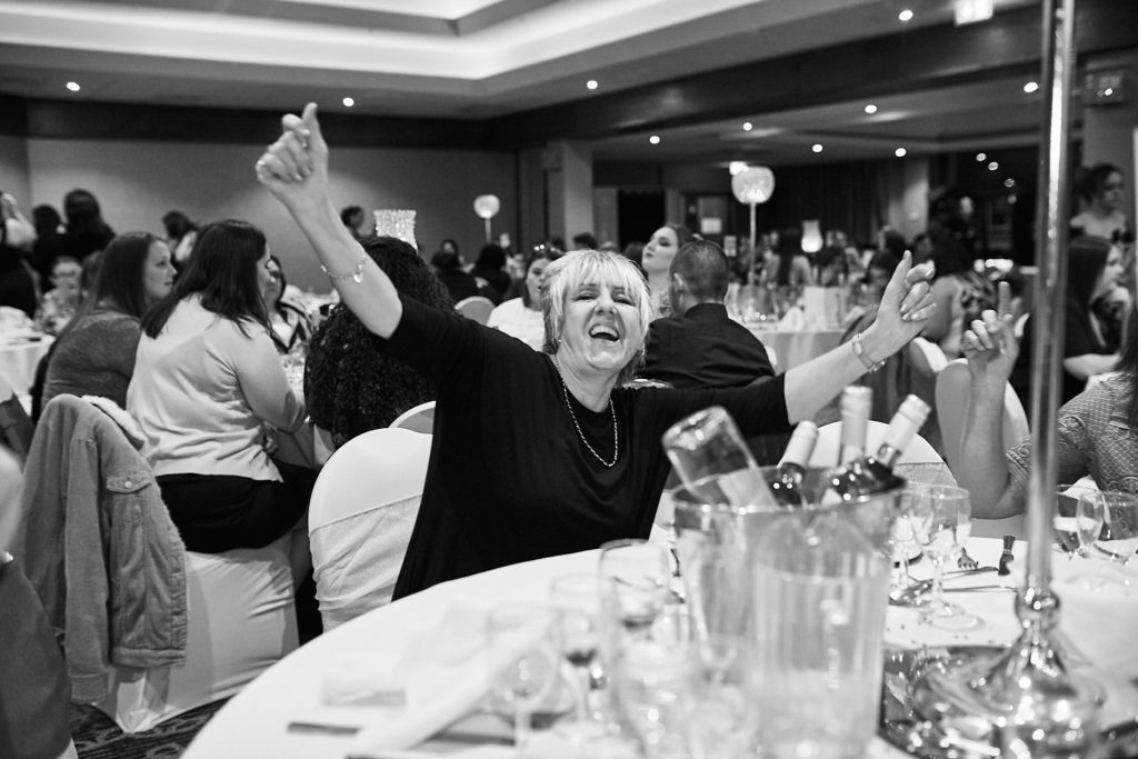 Black and white photo of a table of guests cheering with their arms raised