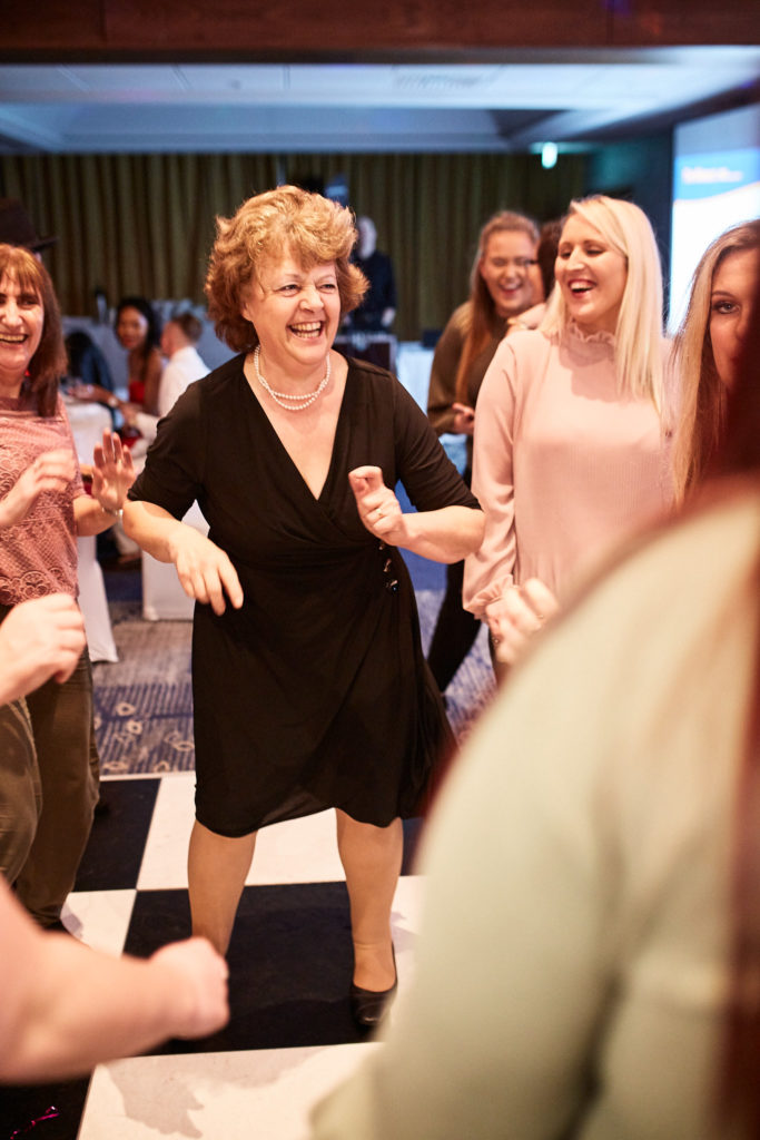 Guest in a black dress laughing as she dances on the chequered dance floor