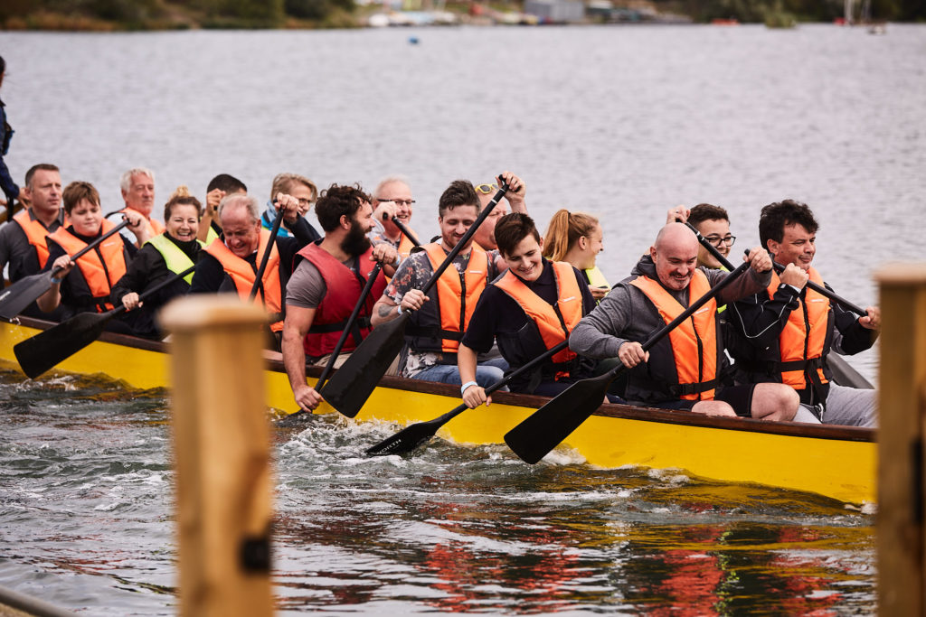 Dragon boat crew in orange life jackets paddling at a charity dragon boat festival at Fairlop Waters