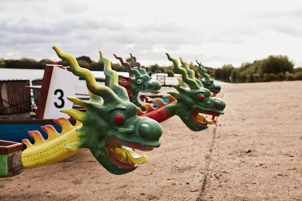 Dragon boats with carved green dragon heads lined up on the shore at Fairlop Waters