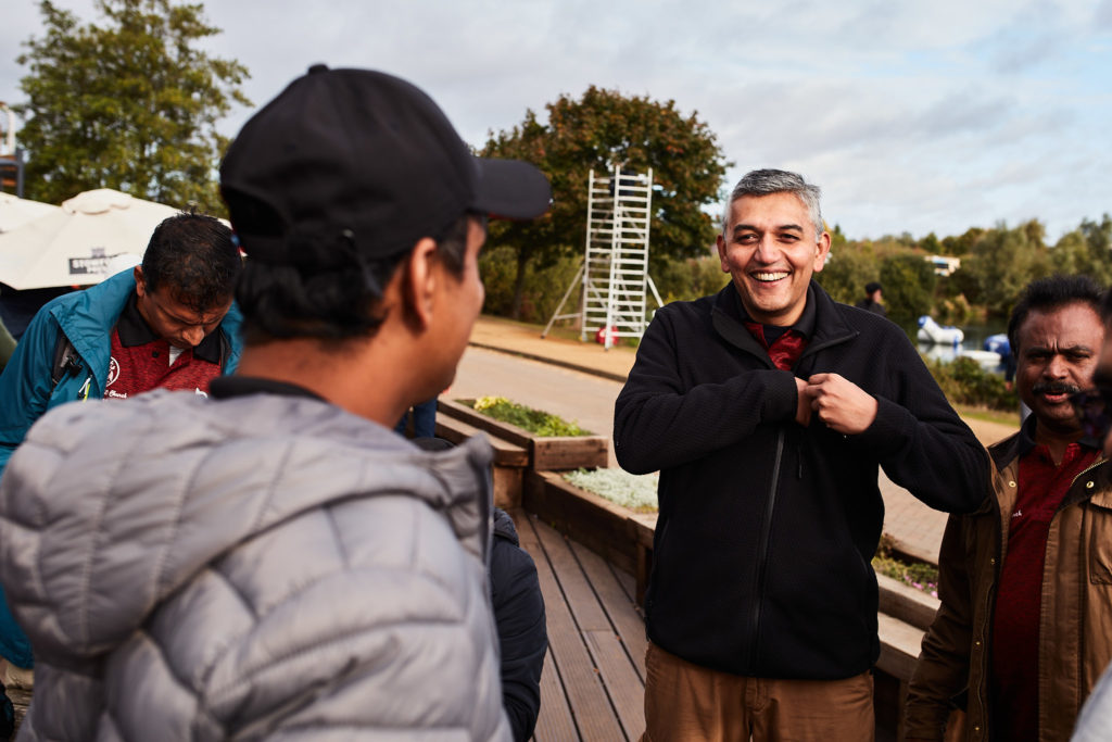 Man in a dark jacket laughing with friends beside the lake
