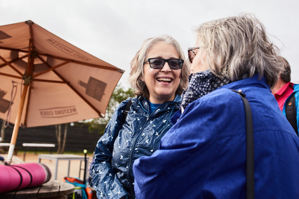Woman in sunglasses laughing with a friend under a parasol