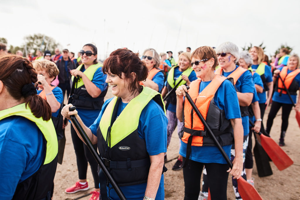 Team in blue shirts and life jackets carrying their paddles to the boats