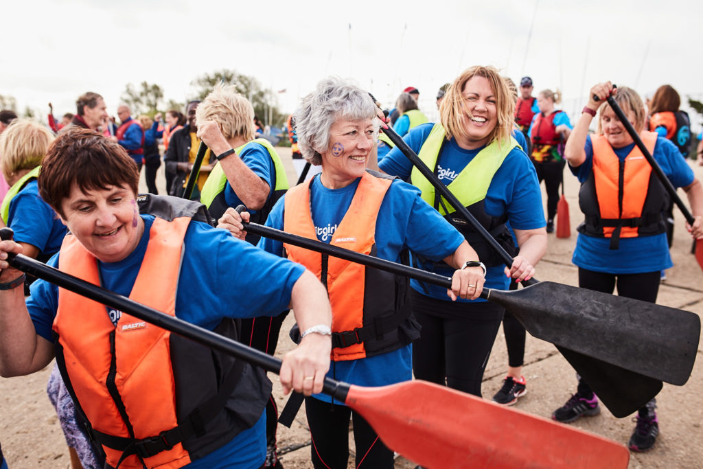Paddlers in orange life jackets laughing as they walk to the start