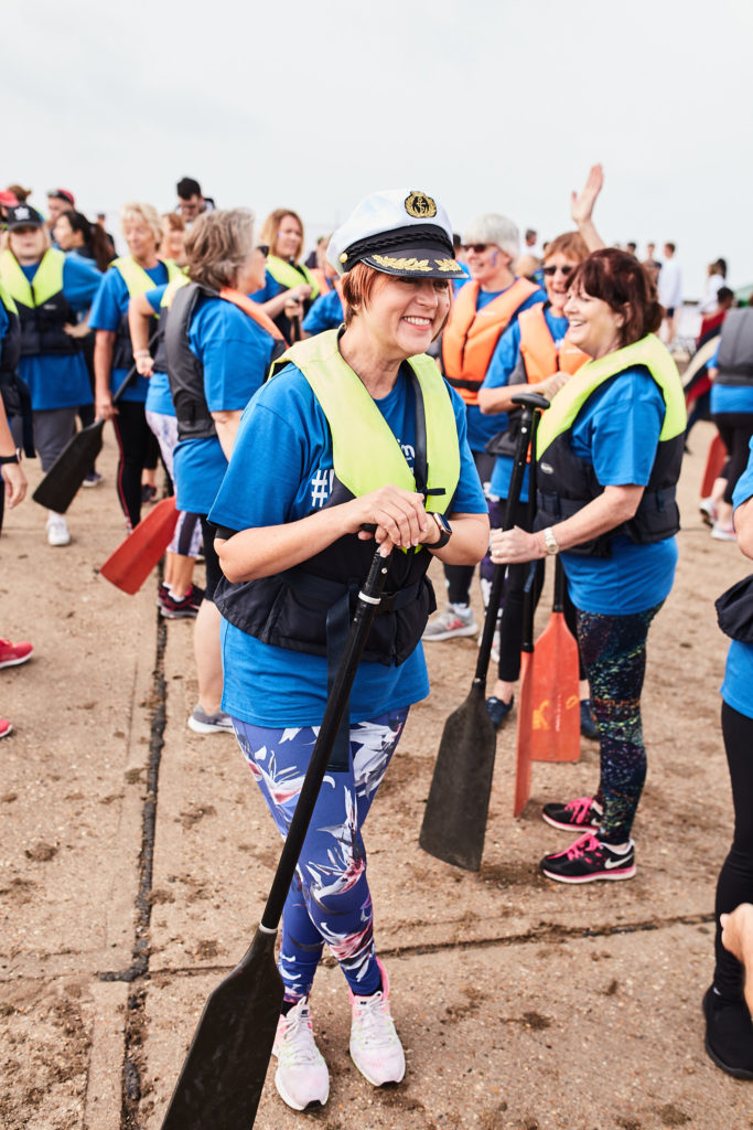 Paddler in a captain's hat walking down to the water with her team