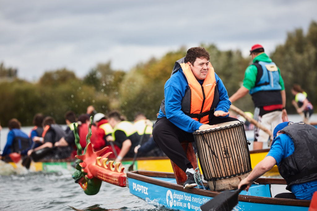 Drummer in a blue jacket beating time at the front of a dragon boat