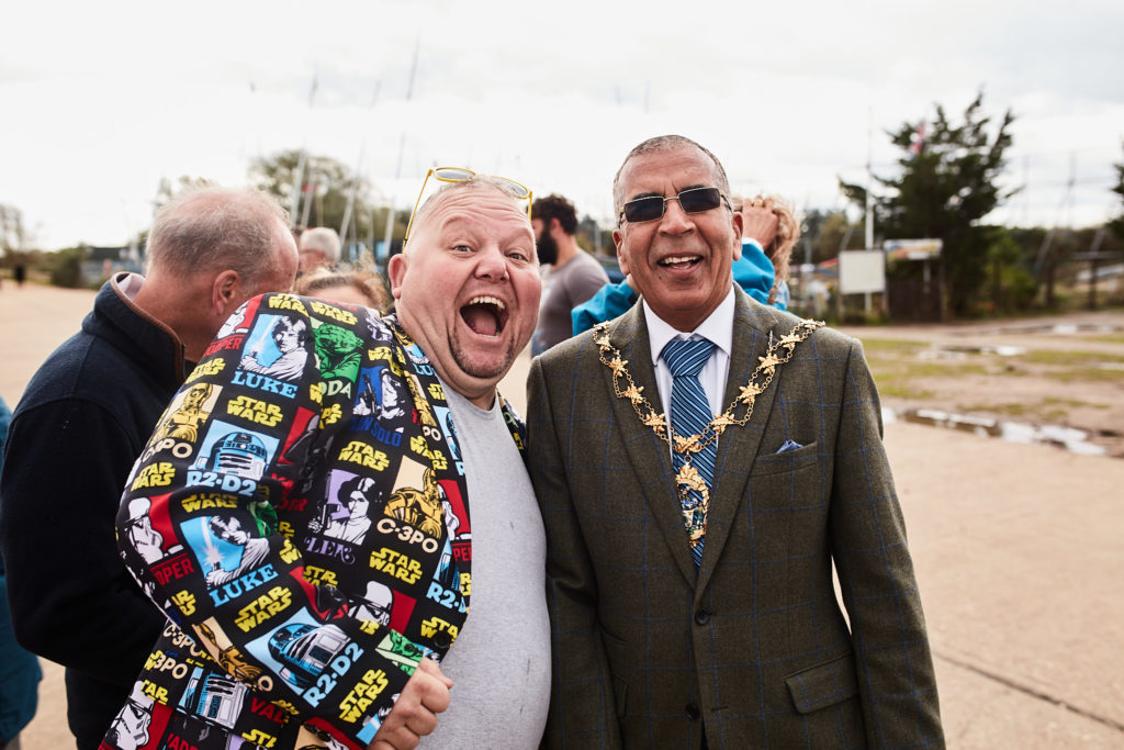 Man in a colourful patterned jacket laughing beside a man in a mayoral chain