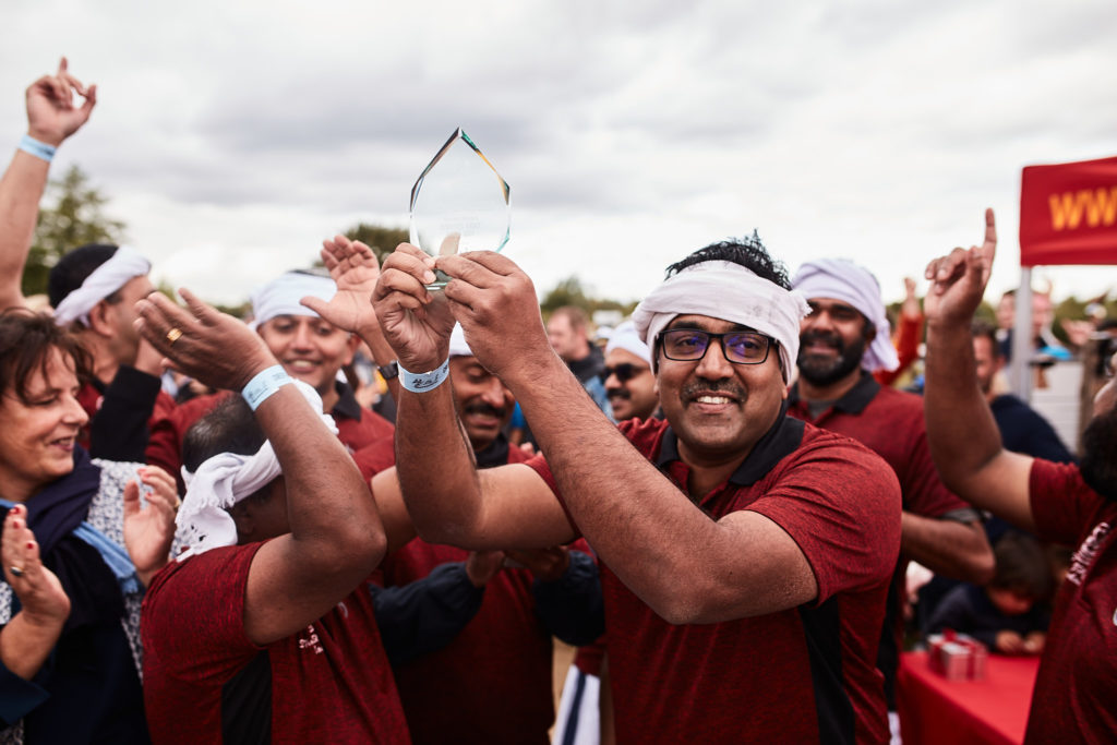 Team in maroon shirts and white headbands cheering as they lift their trophy