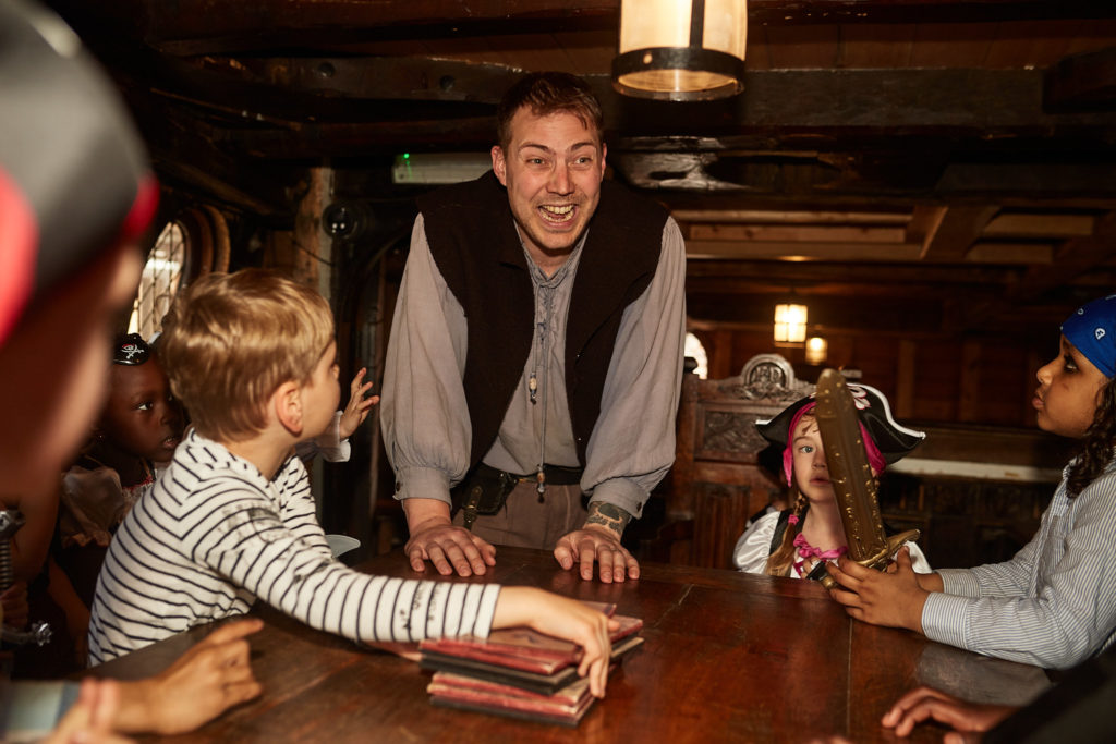 Pirate entertainer leading a game with children below deck on the Golden Hinde