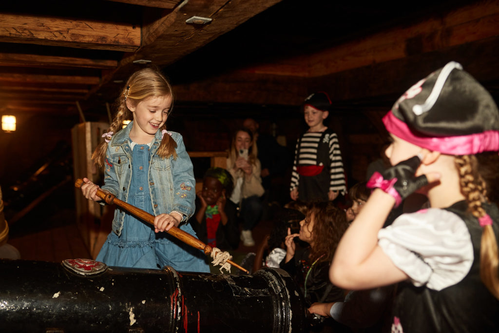Girl holding a toy sword below deck at a pirate birthday party