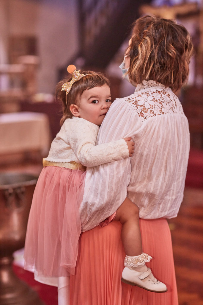 Toddler in a pink skirt looking over her mother's shoulder in church