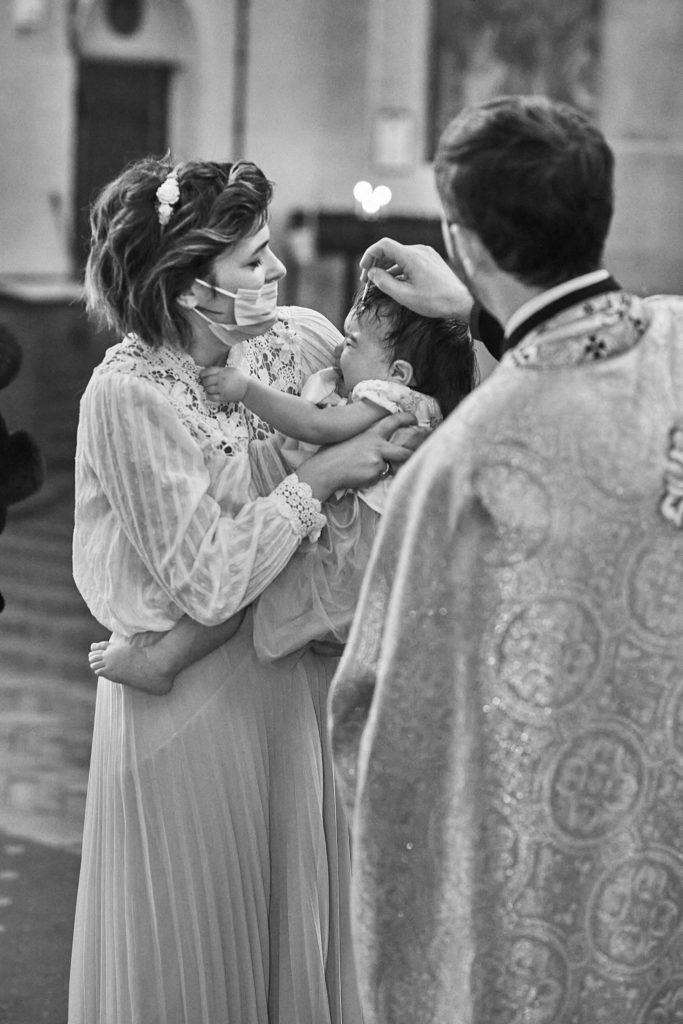Black and white photo of the priest blessing a toddler in her mother's arms