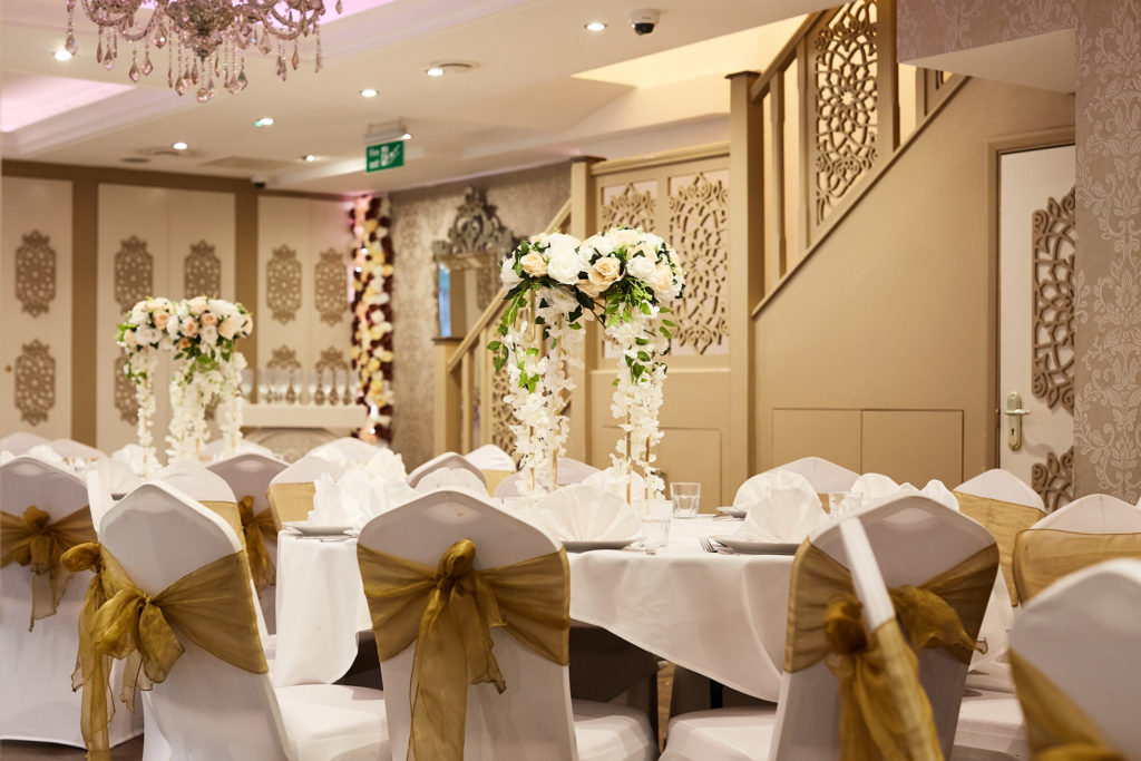 Banquet room set with round tables and gold chair sashes for a mehndi party in Tooting, south London