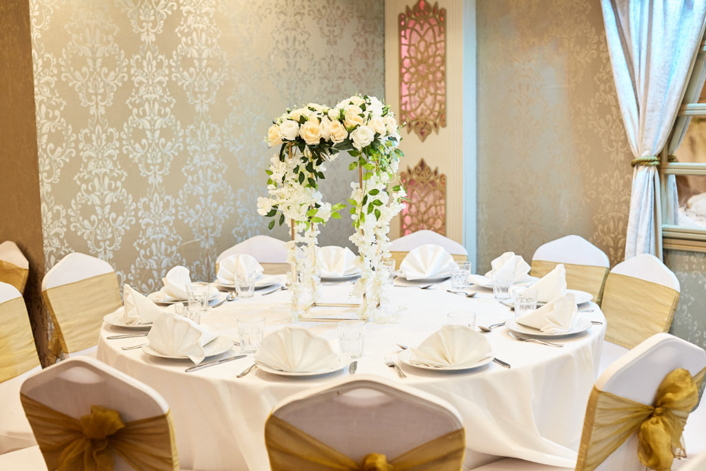 Round table with a tall white flower centrepiece and gold-sashed chairs