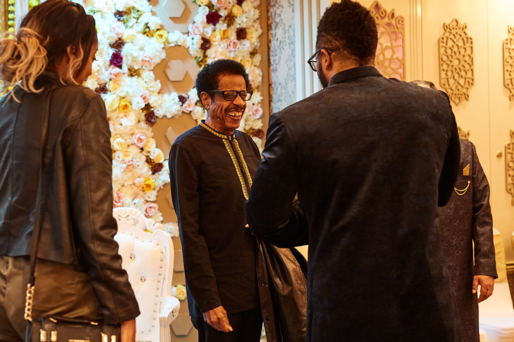 Guests greeting each other in front of a flower wall at the mehndi