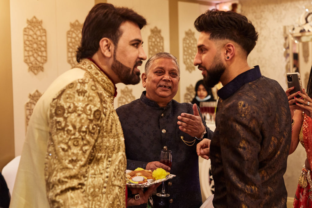 Guests in embroidered sherwanis chatting over plates of food
