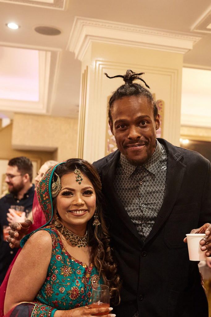 Bride-to-be in a green lehenga and jewelled headpiece smiling with a guest
