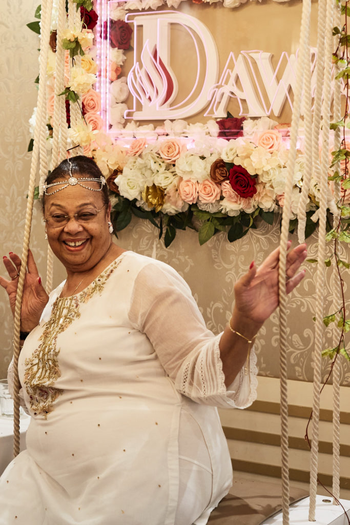 Guest in a white embroidered outfit laughing on a flower-decked swing seat