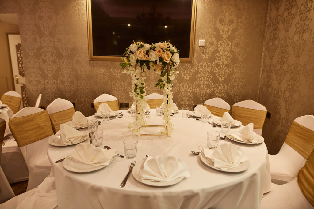 Round table set with white linen and a flower centrepiece in a gold-papered room