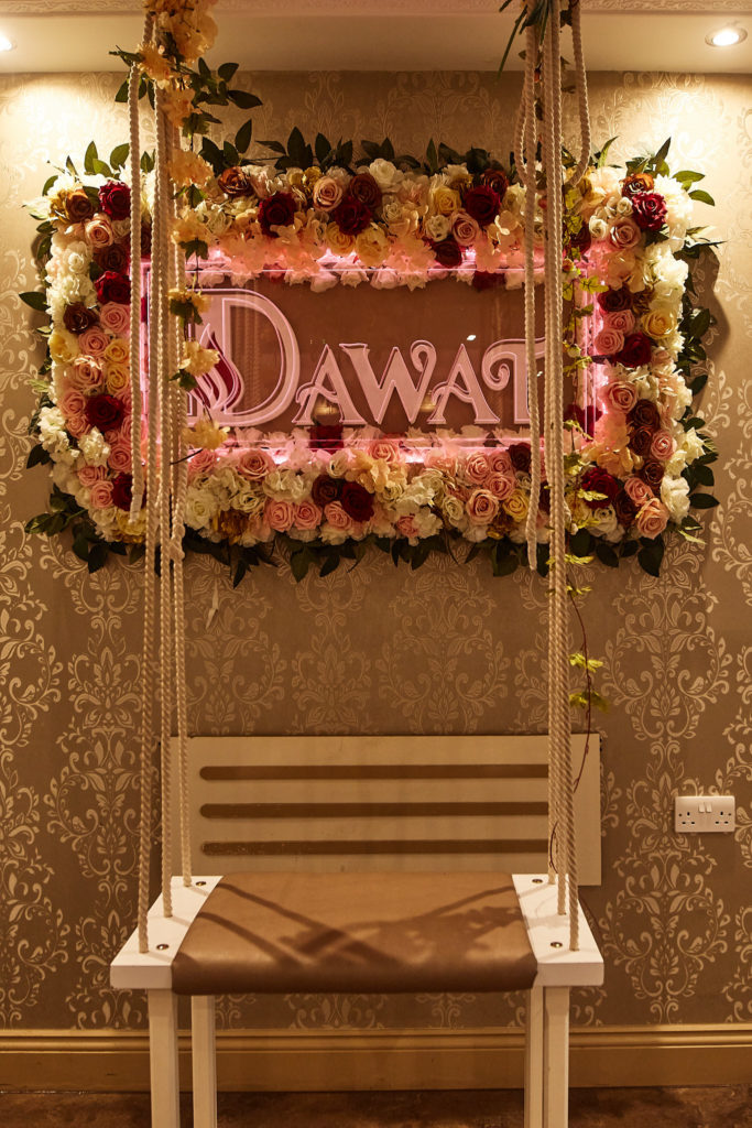 Swing seat beneath a neon sign framed with flowers at the mehndi venue