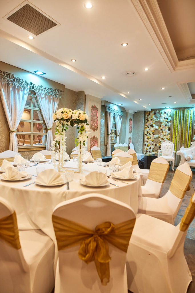 Banquet room with white chair covers and gold sashes, ready for the mehndi party