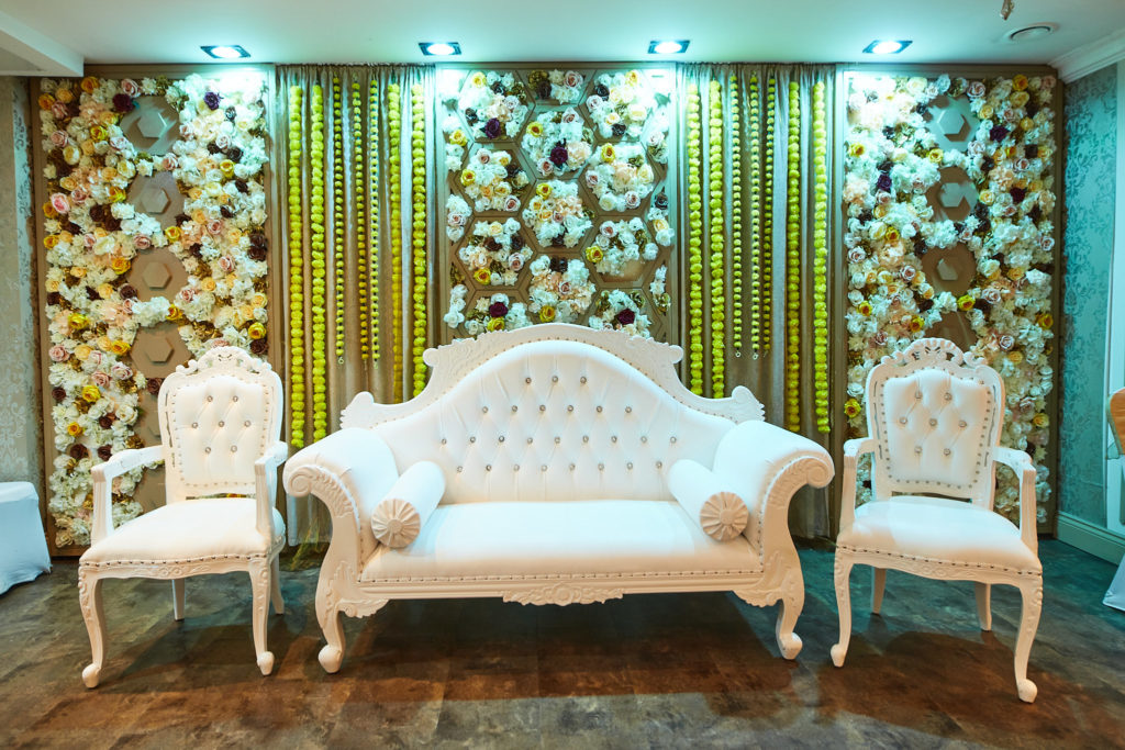 White sofa and chairs on a stage in front of a flower wall