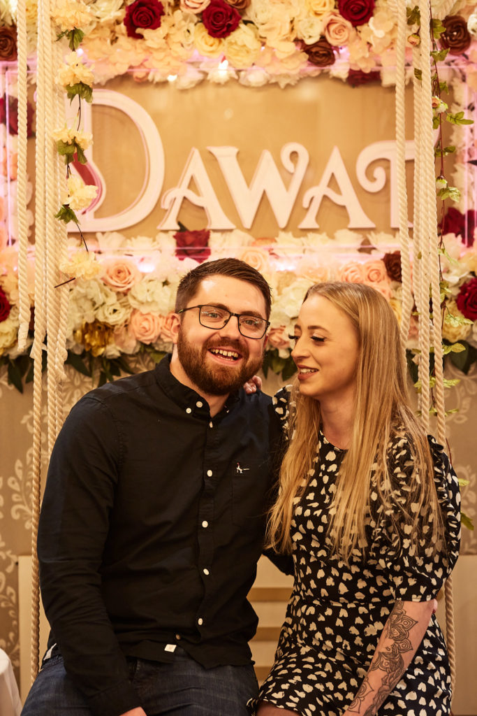 Couple laughing together on the swing seat beneath the neon sign