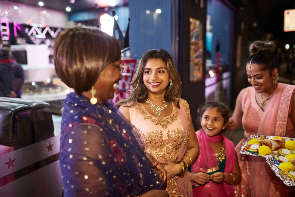 Guests in embroidered outfits holding trays of sweets outside the venue at night