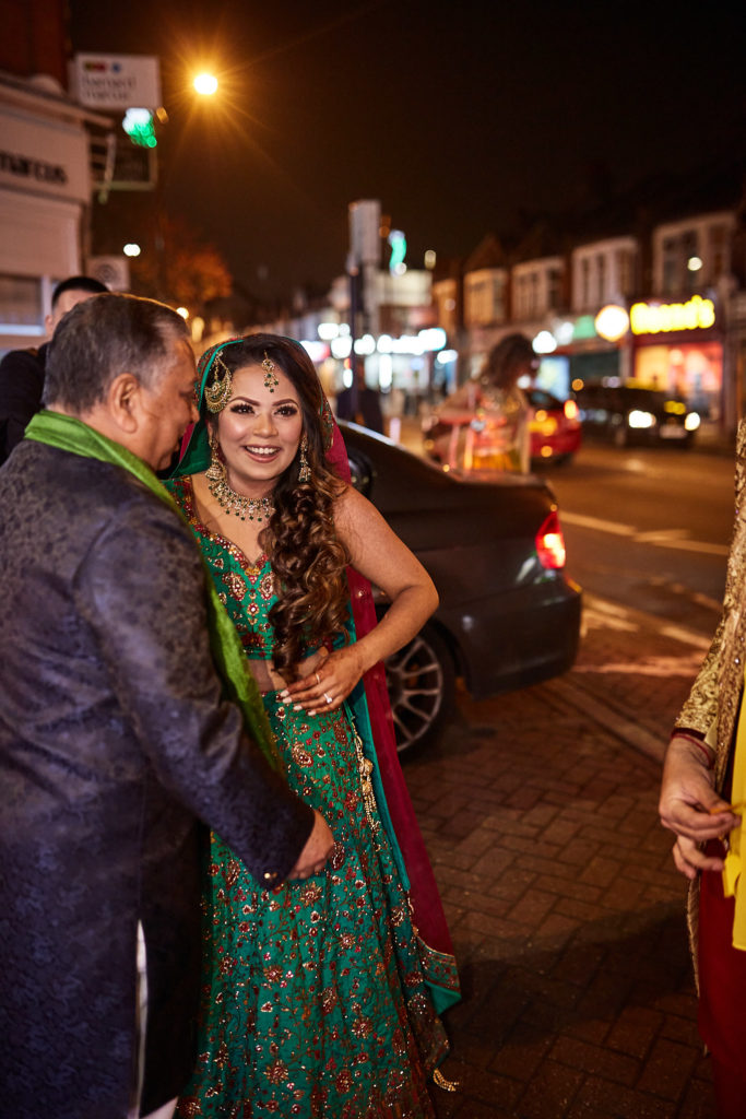 Bride-to-be in a green lehenga laughing with a guest on a Tooting street at night