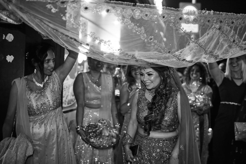 Black and white photo of the bride-to-be walking under a canopy held up by her guests