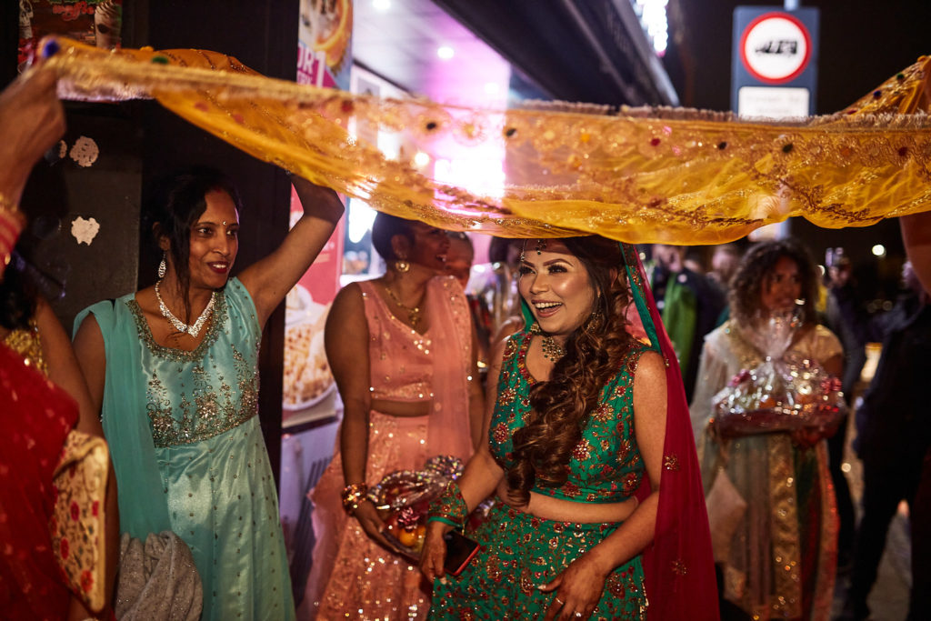 Bride-to-be walking beneath a gold canopy held by her bridesmaids on a London street