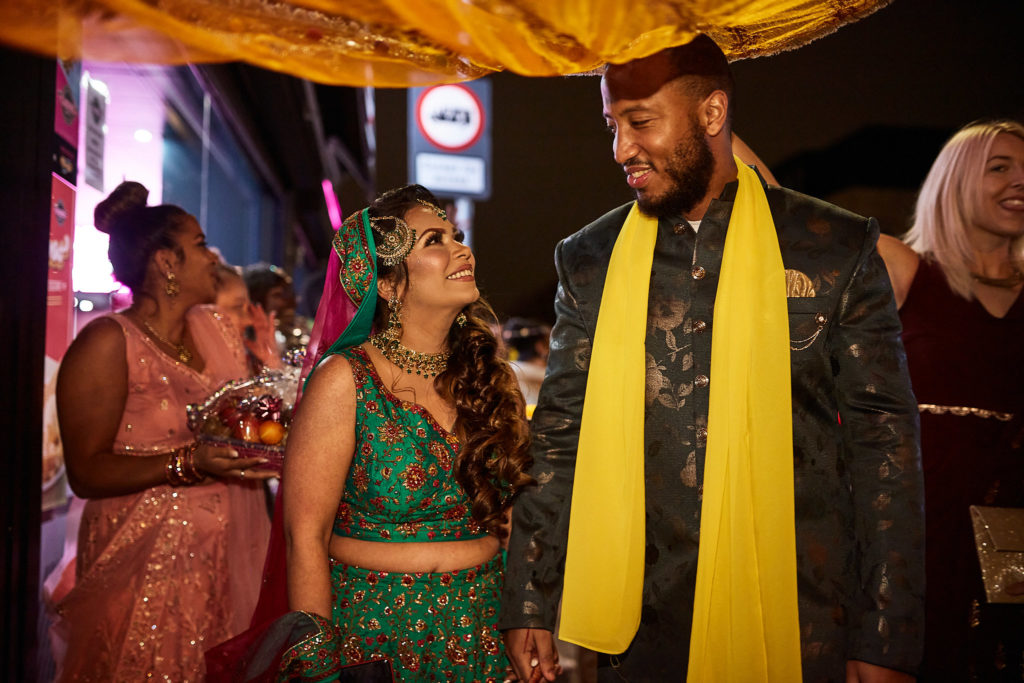 Bride and groom walking together under the canopy in their mehndi procession
