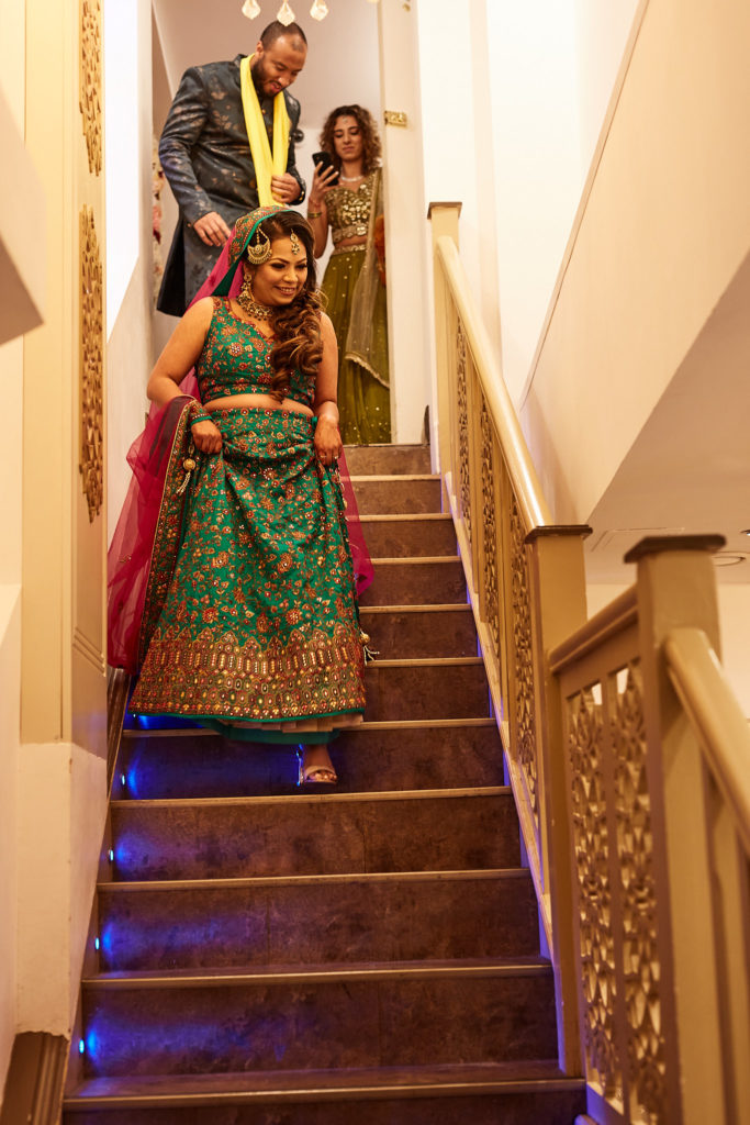 Bride in a green lehenga coming down the stairs with guests behind her