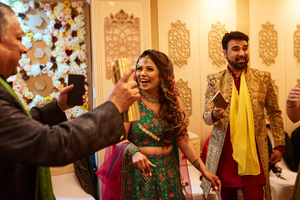 Bride and groom laughing with guests as one films on a phone