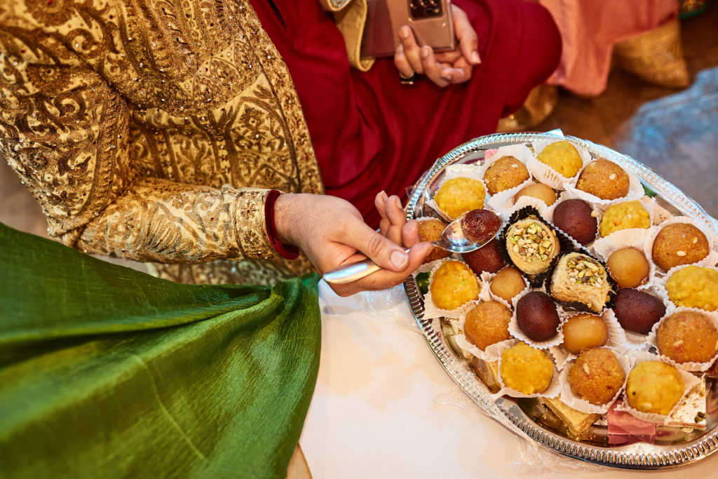 Hands reaching for a tray of sweets during the mehndi ceremony